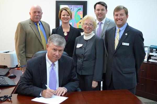 Russell Grizzle, President and CEO of Mannington Mills signs paperwork that allows Mannington to further expand in Madison, GA. Standing are (from left): Bob Hughes, President, Madison-Morgan Chamber of Commerce, Jennifer Nelson, Director of Existing Industry and Regional Recruitment, Georgia Dept. of Economic Development; Susie Haggard, Senior Project Manager, Georgia Dept of Economic Development; Georgia State Senator Burt Jones; Carl Campbell, Senior Project Manager, Georgia Dept of Economic Development